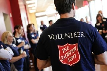 Group of people standing together with the back of a person's shirt in the middle of the frame with Volunteer written on it and the Salvation Army logo
