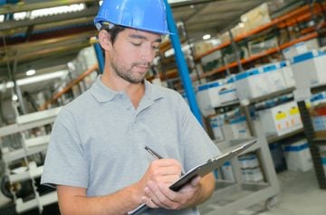Person working in warehouse with hardhat and clipboard